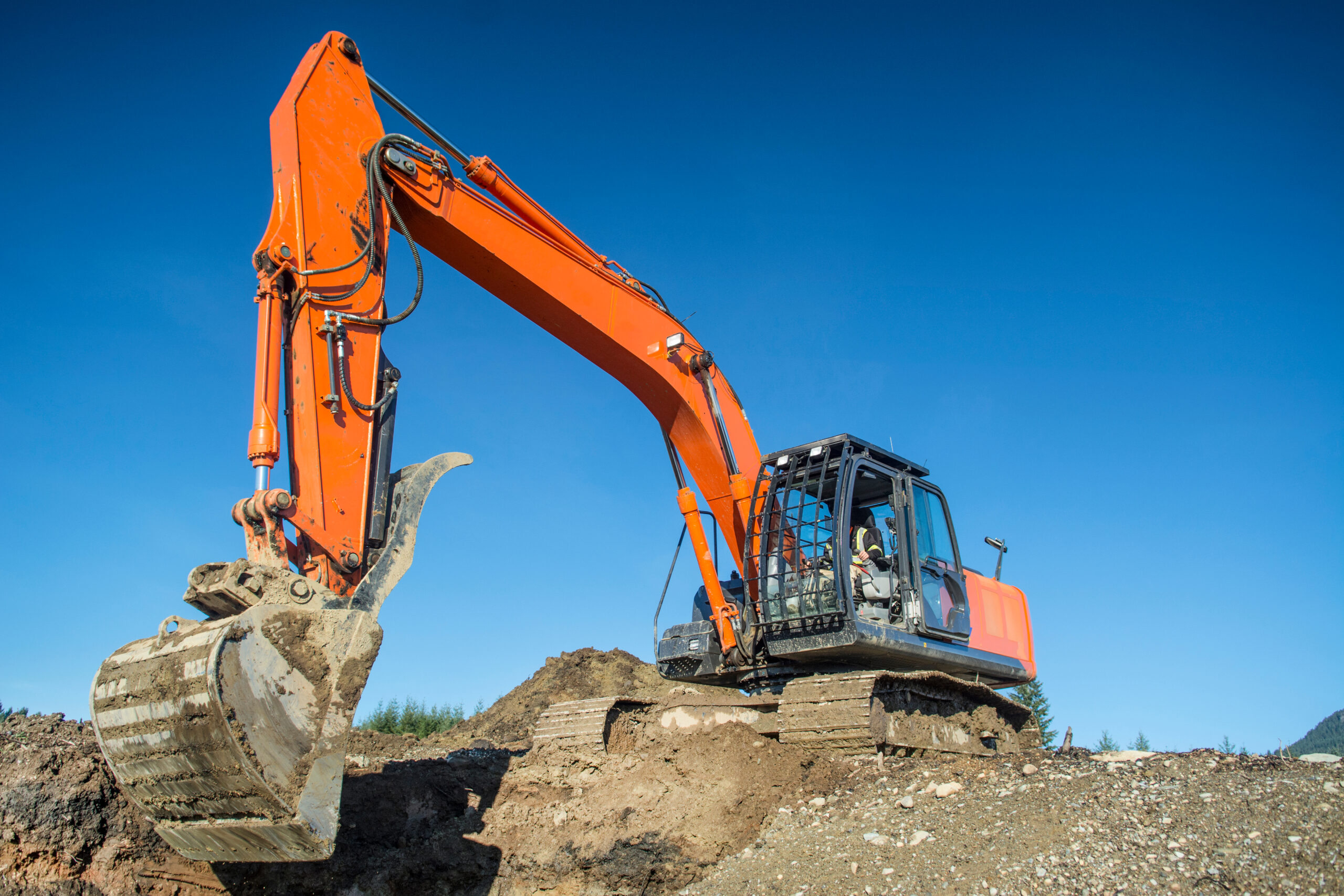 A hydraulic excavator performs earthmoving operations from an elevated spoil pile.